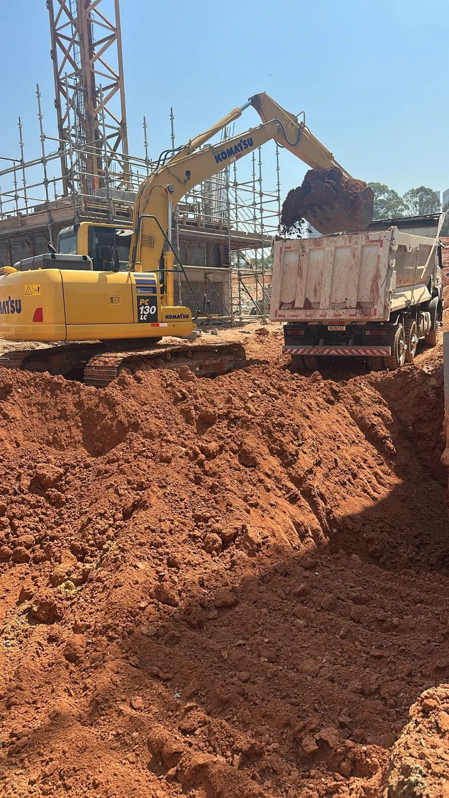 Escavadeira hidráulica da SCAVA carregando caminhão basculante em corte de terreno para obra de construtora em Barueri
