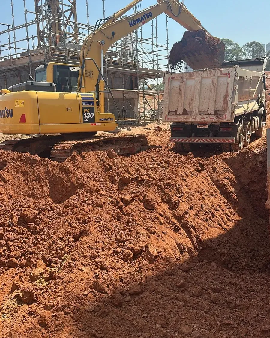 Escavadeira hidráulica da SCAVA carregando caminhão basculante em corte de terreno para obra de construtora em Barueri